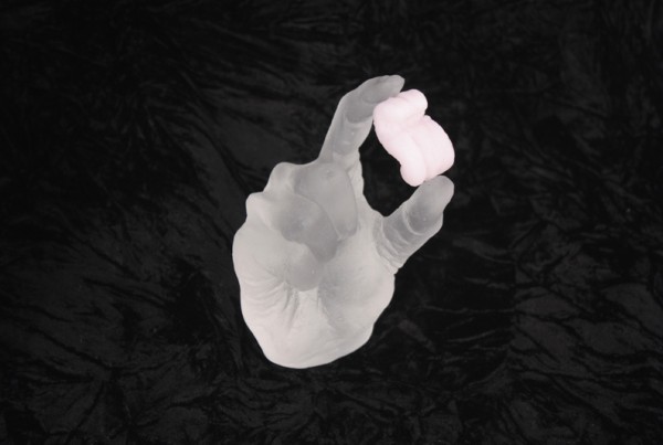 Clear cast glass hand holding a pink cast glass packing peanut